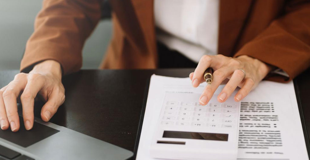Personne consultant un devis de location de van sur tablette avec documents de voyage et calculatrice sur une table, dans un environnement de préparation d'itinéraire